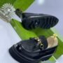 A pair of black loafers with gold accents and Gucci-inspired design, placed on a white surface with green shoe boxes in the background.