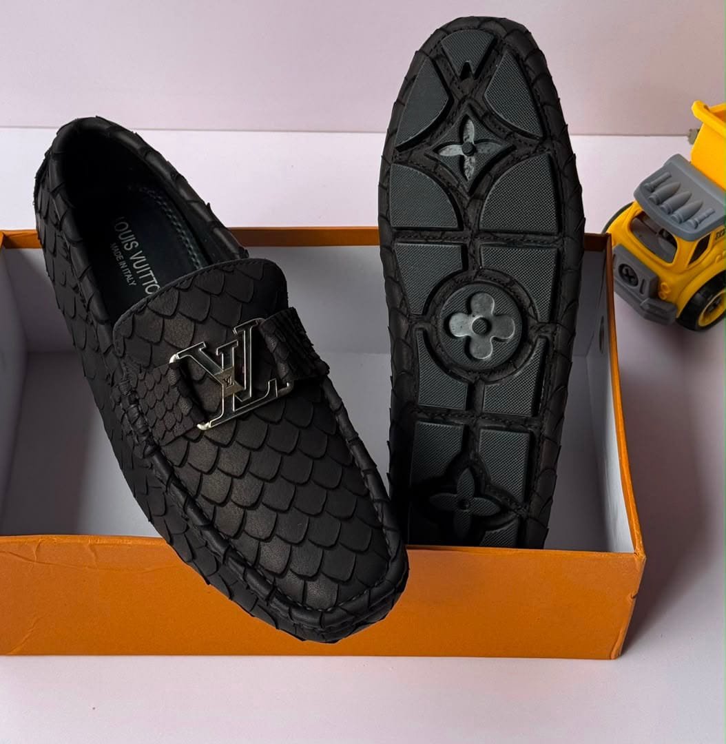 A pair of black snakeskin loafers with a silver buckle, displayed in an orange shoe box with one shoe showing the sole.