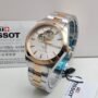 A luxurious Tissot watch with a white face and gold accents, displayed on a white background with its packaging and tags.