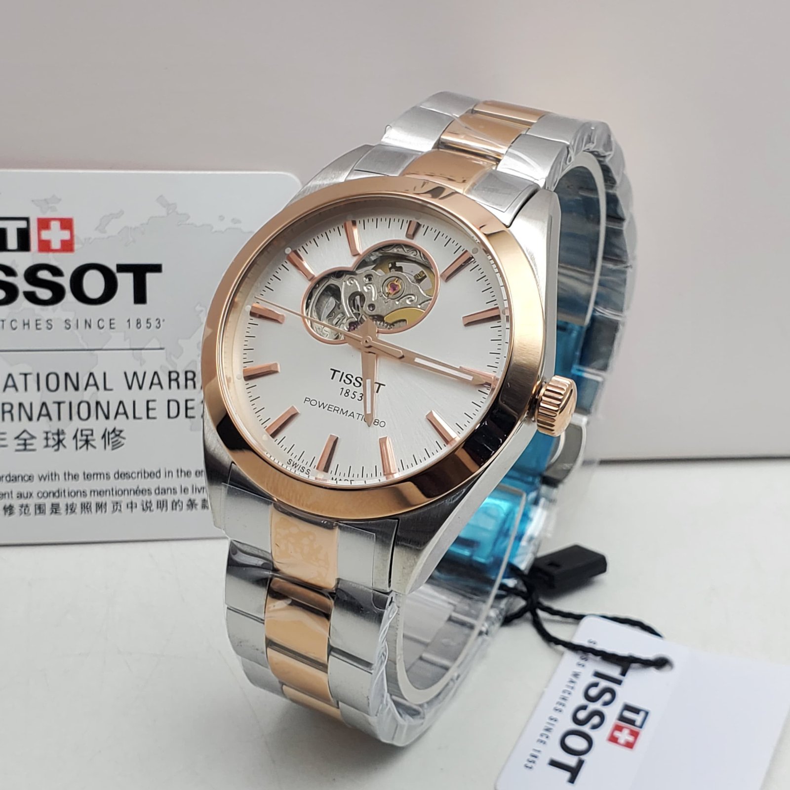 A luxurious Tissot watch with a white face and gold accents, displayed on a white background with its packaging and tags.
