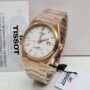 A luxurious rose gold Tissot watch with a white face, displayed on a white background with a warranty card and tag, symbolizing premium quality and style.