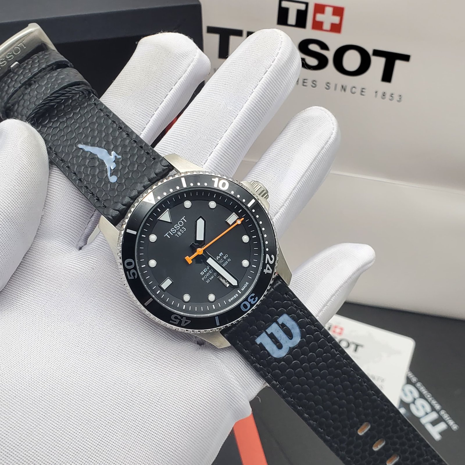 A sleek black Tissot watch with a leather strap, displayed on a white-gloved hand, showcasing its modern design and precise details.