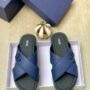 A pair of luxurious blue leather slide sandals with crisscross straps and Dior logo on the insoles, nestled in a white box with a navy blue lid and gold accents.