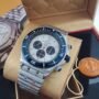 A luxurious silver watch with a white face and blue accents, nestled in a tan box, exuding sophistication and elegance.