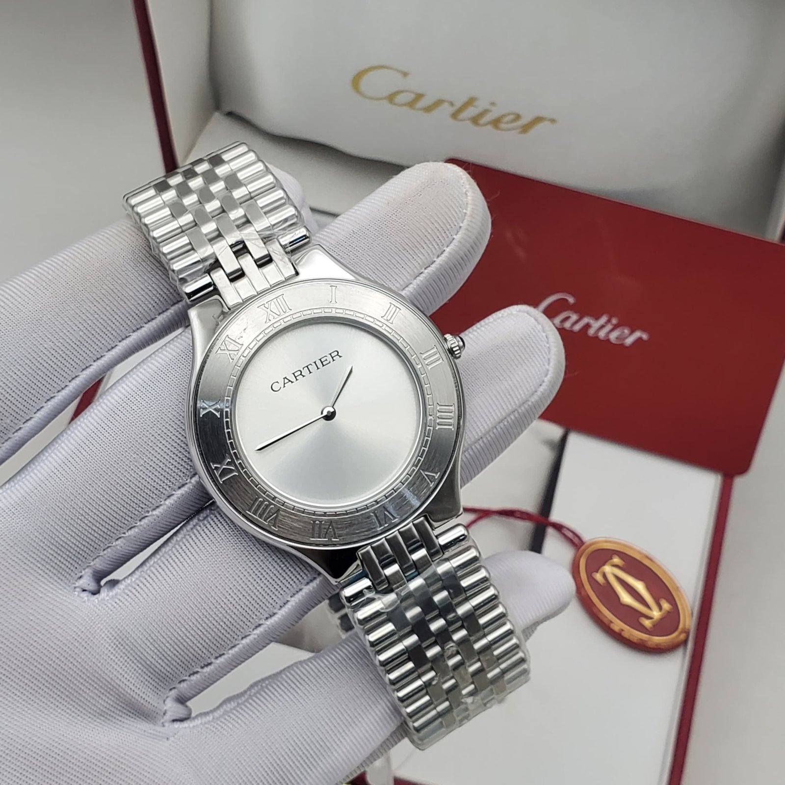 A silver Cartier watch with a Roman numeral face, held by a gloved hand, showcasing its elegant design and craftsmanship.
