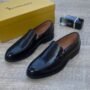 A pair of sleek black leather loafers from Billionaire Italian couture, accompanied by a matching yellow shoe box and a bottle of 212 VIP cologne, exuding luxury and sophistication.