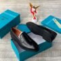 A pair of black leather loafers displayed on a teal shoe box, exuding luxury and sophistication.